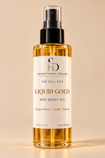 A 4 oz bottle of Sensational Deluxe 'The Fall Edit' Liquid Gold Dry Body Oil, featuring a clear bottle filled with golden oil, a black spray pump, and a cream-colored label, set against a warm beige background.